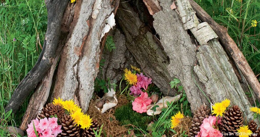 Fairy house built from bark sticks and pinecones decorated with pink flowers in a garden