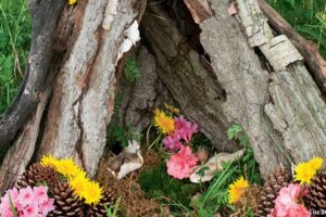 Fairy house built from bark sticks and pinecones decorated with pink flowers in a garden
