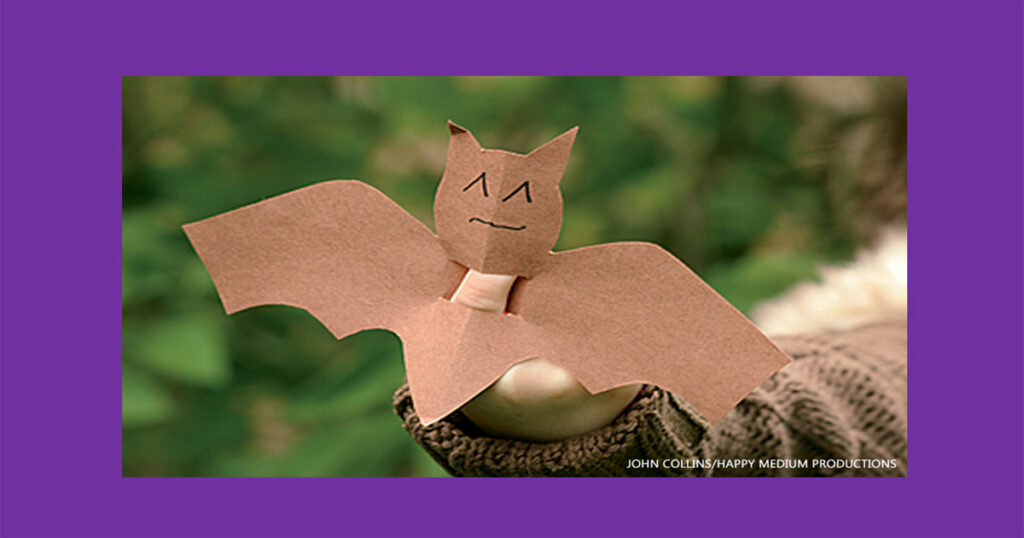 Brown paper bat finger puppet worn on a child's finger outdoors