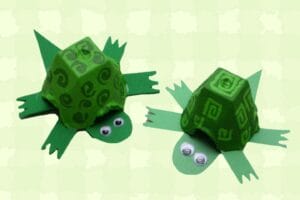 Two green painted egg carton turtles with googly eyes on green background
