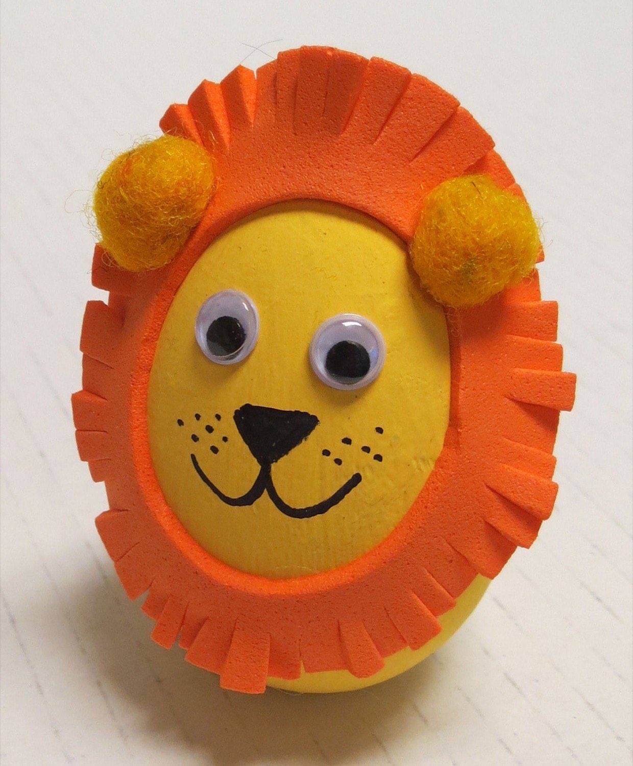 Yellow painted wooden egg lion with orange fringed paper mane fuzzy ears and googly eyes