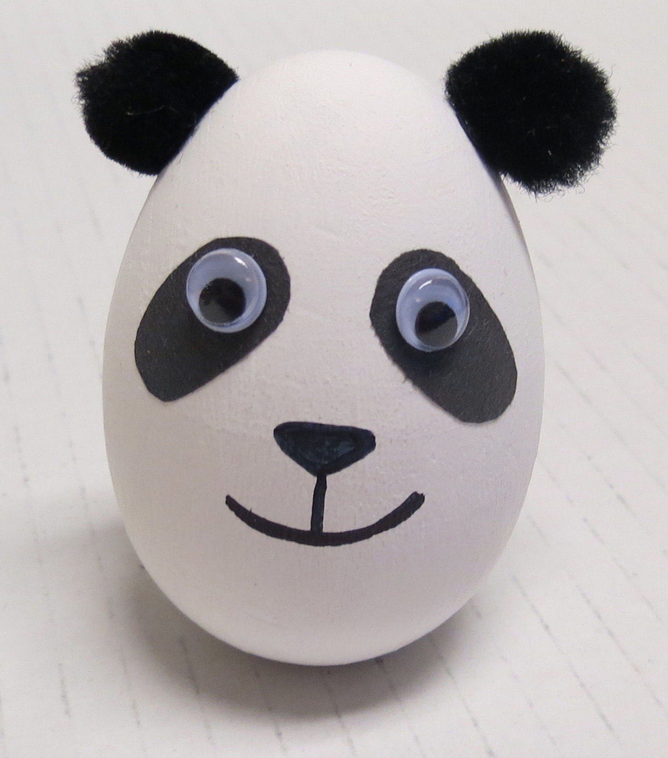 White painted wooden egg panda with black paper eye patches fuzzy ears and smiling face