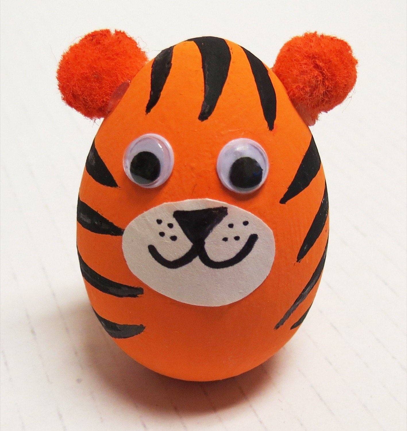 Orange painted wooden egg tiger with black stripes red pom pom ears and white muzzle