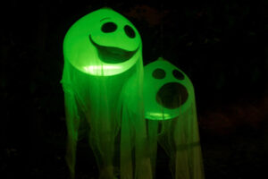 Two glowing green balloon ghosts with spooky faces floating in the dark on Halloween