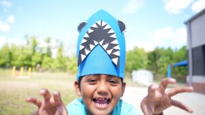 Close-up of a child roaring playfully while wearing a handmade blue shark hat