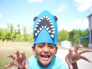 Close-up of a child roaring playfully while wearing a handmade blue shark hat