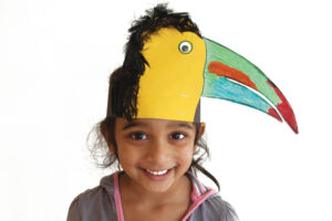 Smiling girl wearing a colorful paper toucan headband with green and red bill and feathers