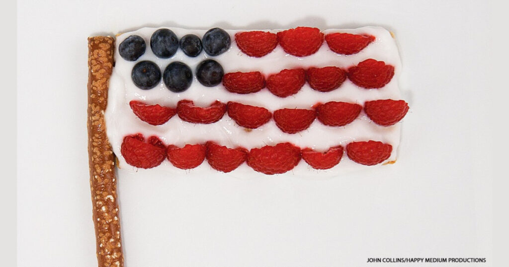 American flag snack made from graham cracker yogurt raspberries and blueberries on pretzel stick