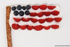 American flag snack made from graham cracker yogurt raspberries and blueberries on pretzel stick