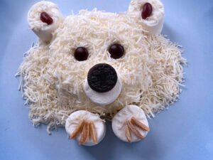 Polar bear ice cream treat with coconut fur and marshmallow paws on a blue plate