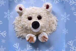 Polar bear face made from ice cream and coconut with an Oreo nose on a snowflake background