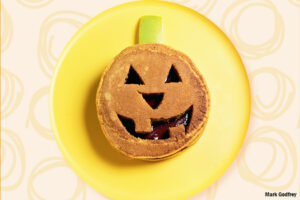 Pumpkin pancake decorated as a jack-o-lantern face on a yellow plate
