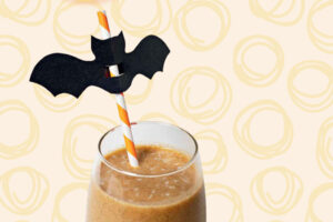 Pumpkin pie smoothie in a glass with an orange striped straw and paper bat decoration