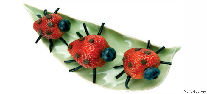 Three strawberry ladybugs with blueberry heads and licorice legs on a green leaf dish