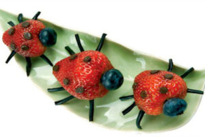 Three strawberry ladybugs with blueberry heads and licorice legs on a green leaf plate