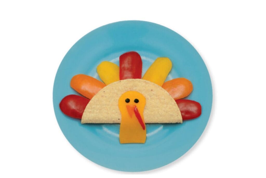 Turkey shaped taco on blue plate with colorful pepper slices as tail feathers and cheese head