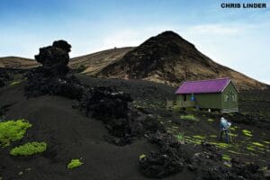 Small green research hut on black volcanic lava landscape of Surtsey with scientist walking