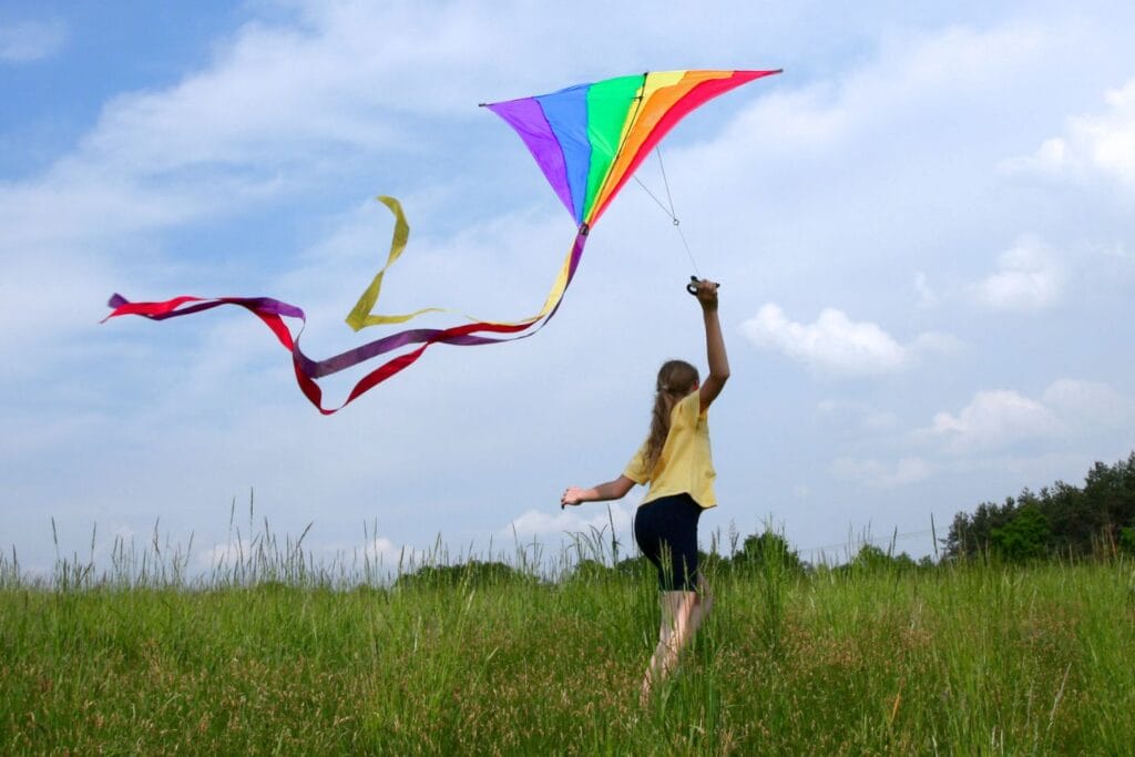 girl flying bright colorful kite in a grassy field on a sunny day