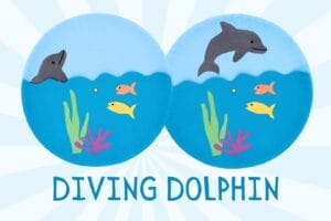 side-by-side views of a children's paper plate craft featuring a gray dolphin diving into blue ocean water above colorful fish, seaweed, and coral. The finished craft is labeled "Diving Dolphin."