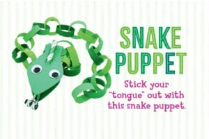 Girl blowing a party horn snake tongue while holding up a green paper chain snake puppet