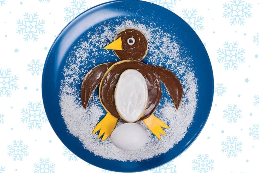 pancake shaped like a penguin with coconut snow on a blue plate