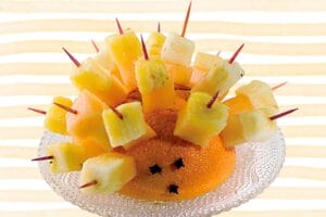 Spiky fruit hedgehog made from half an orange with toothpick fruit cube spines on glass plate